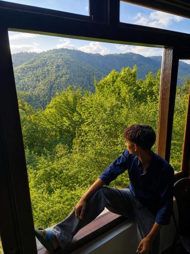a man sitting in a window looking out at the mountains at A Home Above the Clouds Riturain Mukteshwar in Mukteshwar