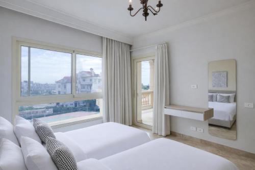 a white bedroom with two beds and a large window at El Safwa Resort New Cairo in Cairo