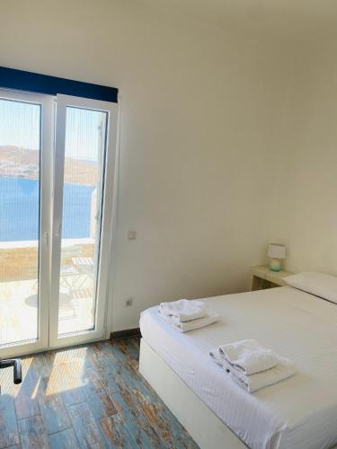 a white bedroom with a bed and a large window at Sto Faro - Blue in Kithnos