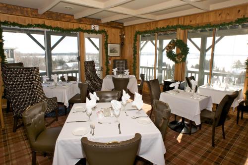 a restaurant with white tables and chairs and windows at Eganridge Resort, Golf Club & Spa in Bobcaygeon