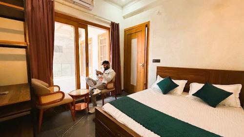 a man sitting in a room with a bed and a window at Yes Hotel By The Ganges Rishikesh in Rishīkesh