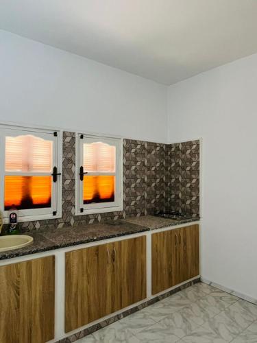 a kitchen with two windows and a sink at Appartement Al Hanine in Douz
