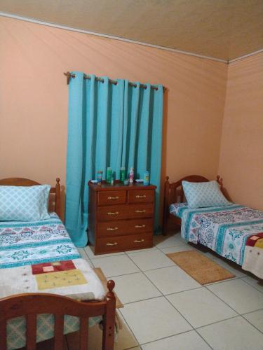a bedroom with two beds and a dresser and blue curtains at Tessa's Inn in Arima