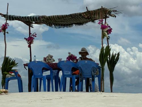 a man sitting at a table with blue chairs on the beach at Funzi Beach Resturant in Funzi