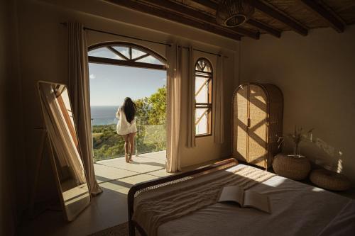 a woman standing outside a window looking out at the ocean at Native Villa with Pool at Kalumo Lodge in Oslob