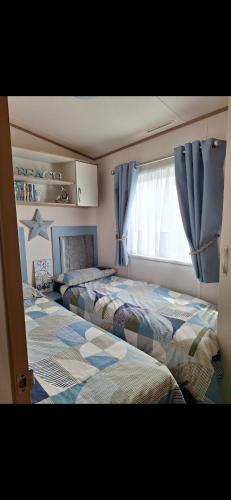 two beds in a bedroom with blue curtains and a window at Perranporth Cornwall in Perranporth