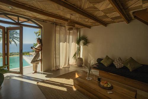 a woman standing in a living room looking out at the ocean at Native Villa with Pool at Kalumo Lodge in Oslob