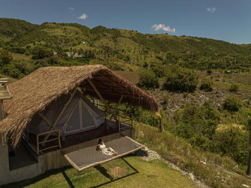 a person sitting on a bed in front of a hut at Glamping at Kalumo Lodge - Tent 1 in Oslob