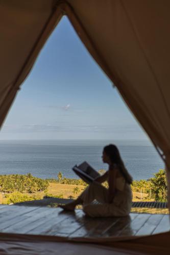 a woman sitting in a tent looking out at the ocean at Glamping at Kalumo Lodge - Tent 1 in Oslob