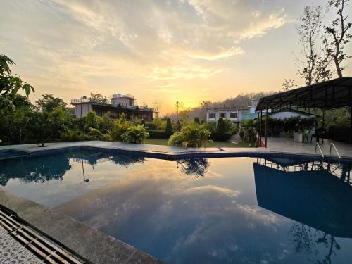 a swimming pool with a sunset in the background at Corbett Mid Forest House - 1 Min Walk from Dabka River in Rāmnagar