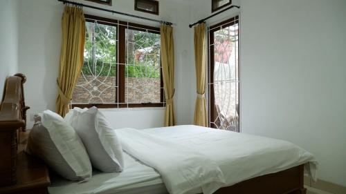 a bed with white sheets and pillows in a room with windows at villa NC3 31 Kota Bunga in Cikundul