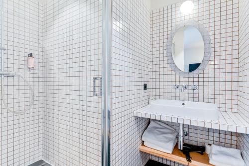 a white tiled bathroom with a sink and a mirror at Hotel Habituel in Paris