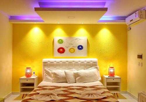 a bedroom with a yellow wall with a bed and two lights at Villa Araçà - Boutique Hotel in Lauro de Freitas