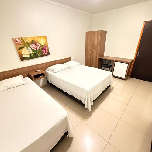 a bedroom with two beds and a painting on the wall at Hotel Rio Grande in Dourados