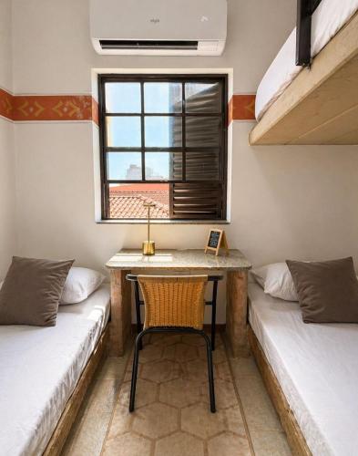 a room with two beds and a table and a chair at Unidade 2 - GoHost Suítes in Ribeirão Preto