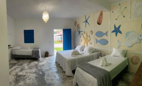 a room with two beds and a wall with paintings at Pousada Villa Japa in Maragogi