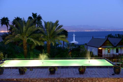 a swimming pool at night with palm trees and a lighthouse at Orchid Eilat Hotel in Eilat