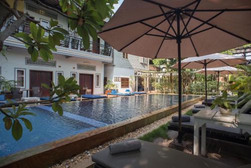 a pool with chairs and an umbrella next to a house at The Local Time Village in Siem Reap