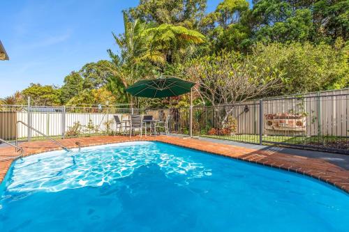 a swimming pool with a table and an umbrella at Brodie Getaway in Coffs Harbour