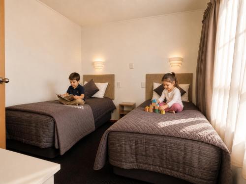 two children sitting on beds in a hotel room at Teal Motor Lodge in Gisborne