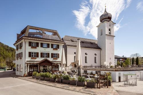 a white building with a clock tower next to a street at Kirchenwirt in Strobl