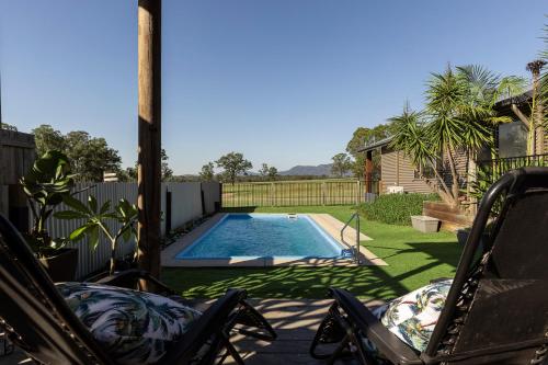 a swimming pool in a yard with two lawn chairs at Wallaby Lodges in Pokolbin