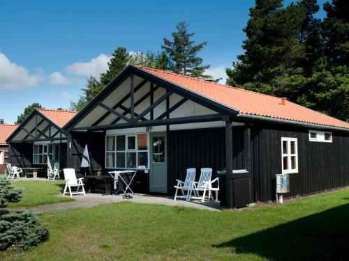 a black cottage with white chairs in the yard at 6 person holiday home in Væggerløse in Bøtø By