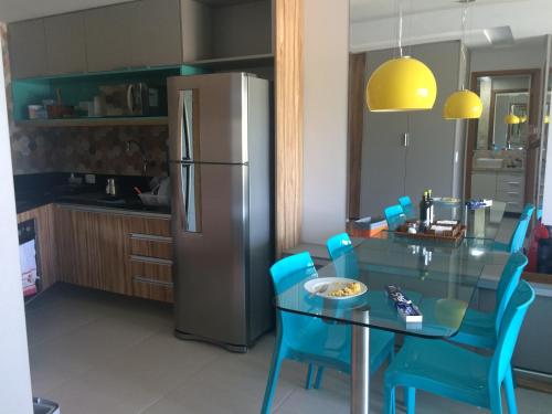a kitchen with a glass table with blue chairs and a refrigerator at Flat Carneiros Beach Resort in Tamandaré