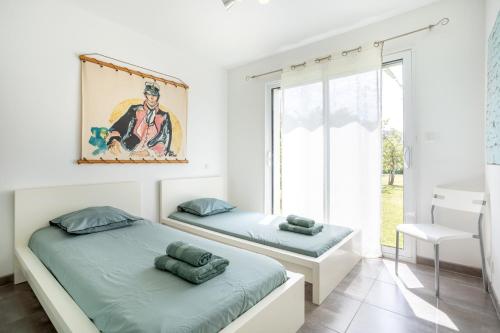 a white bedroom with two beds and a window at La maison du verger in Loctudy