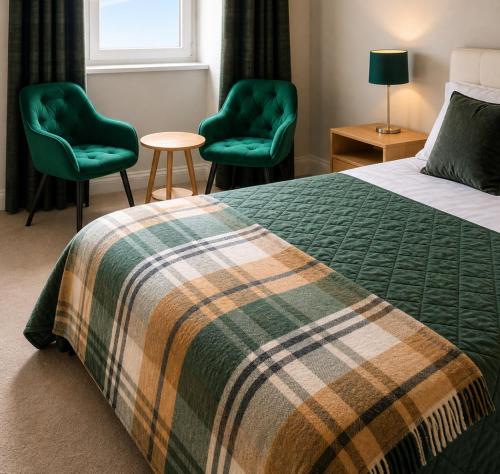 a bedroom with a bed and two green chairs at Station Hotel in Burghead