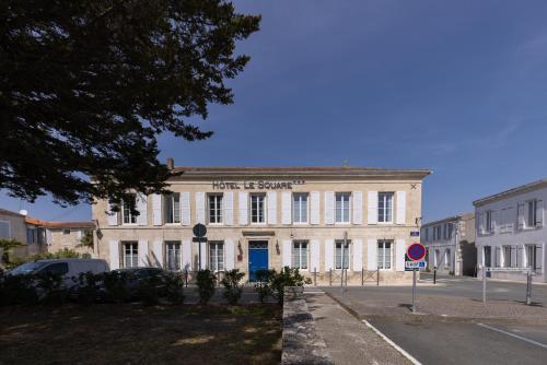 a large white building with a blue door on a street at Hôtel Le Square in Saint-Pierre-dʼOléron