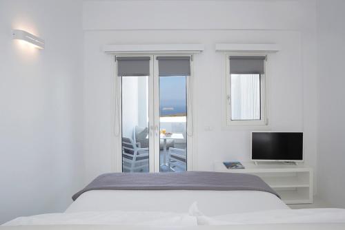 a white bedroom with a bed and a television at Blue Vice Megalochori in Megalochori