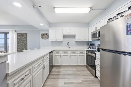 a kitchen with white cabinets and a stainless steel refrigerator at Sandy Bits Oceanfront Premium Condo with Pool in Myrtle Beach
