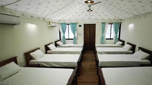a row of beds in a room with blue curtains at Krishna's den- a cottage retreat a Gaudham Periyar Farmstay in Jambhulpāda