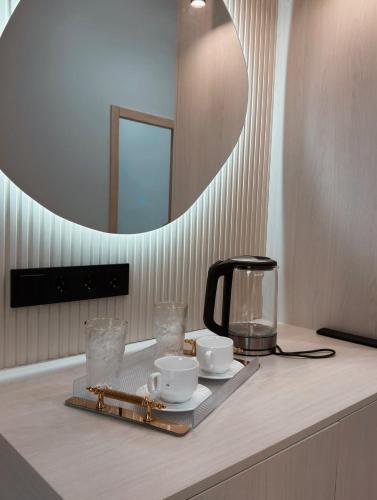 a table with a coffee maker and cups and a mirror at Small Cozy Spa Hotel in Aktobe