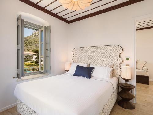 a white bedroom with a white bed and a window at Bellevalia Hydra in Hydra