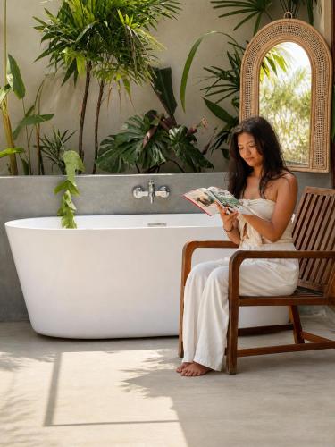 a woman sitting in a chair reading a magazine in a bathroom at Zen Koggala by Sugar Coliving in Habaraduwa Central