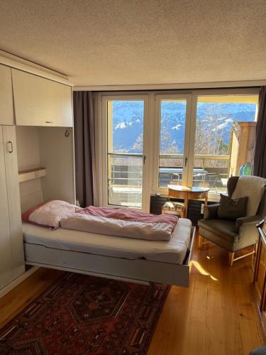 a bedroom with a bed and a chair and windows at Blüemlisalp 712 Studio in Beatenberg