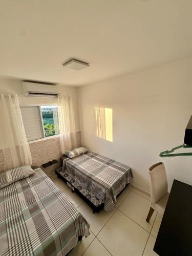 a bedroom with two beds and a desk and a window at Apartamento 2 Quartos Aconchegante - Ar Condicionado nos Quartos - 1 Cama Casal - 2 Camas de Solteiro com Auxiliar - Cozinha Completa - Estacionamento Gratuito in Três Lagoas