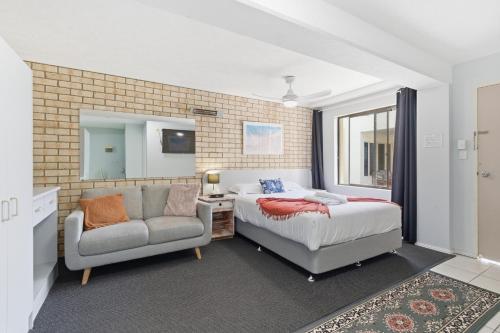 a bedroom with a bed and a couch and a chair at Ocean Parade Motel in Coffs Harbour