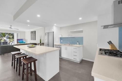 a white kitchen with a counter and stools in it at Turquesa Tides - Beachfront Resort Living in Palm Cove