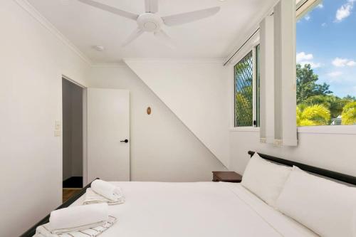 a white bedroom with a bed with a ceiling fan at Tropical Cove at Trinity Beach with Lagoon Pool in Trinity Beach