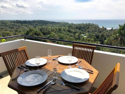 a wooden table with plates and wine glasses on a balcony at Lara's place in Unawatuna