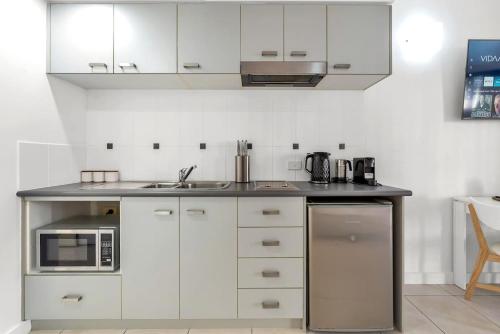 a kitchen with white cabinets and a sink and a microwave at Lagoon Lookout - Poolside Studio near Trinity Beach in Trinity Beach