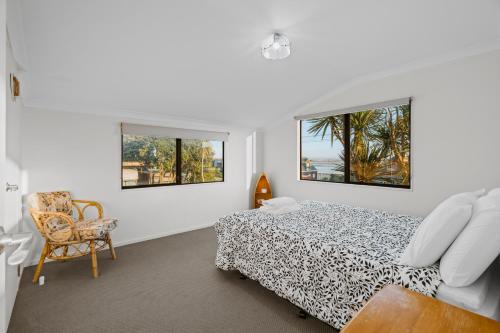 a bedroom with a bed and a chair and two windows at Waterfront location with estuary outlook and ocean beach access - sleeps 19 in Pukehina