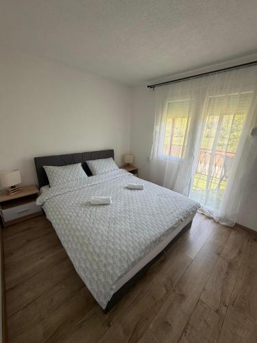 a bedroom with a large bed with white sheets and wood floors at Vikendica Markić in Šipovo