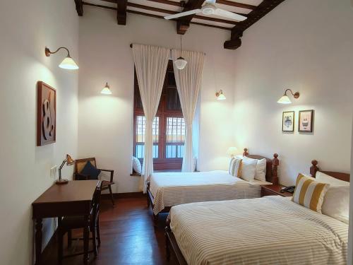 a hotel room with two beds and a desk and a window at Ezekiel House Residence in Cochin
