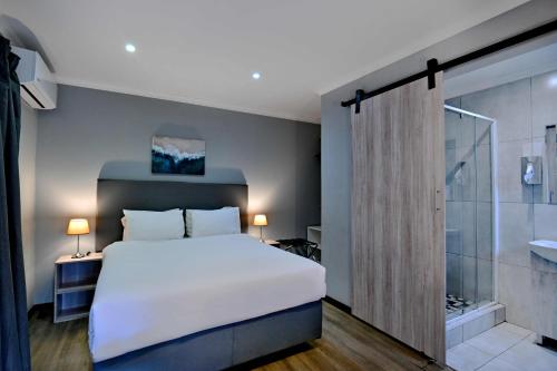 a bedroom with a large white bed and a bathroom at BON Hotel Rustenburg in Rustenburg