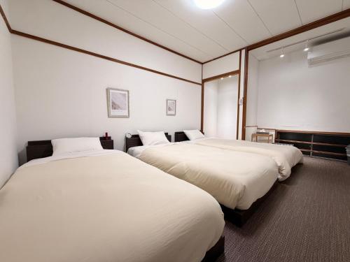 two beds in a room with white sheets at ura San Jose トリプルルーム in Okayama