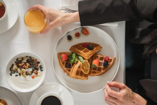 a table with a plate of waffles and a bowl of fruit at Savoia Hotel Rimini in Rimini